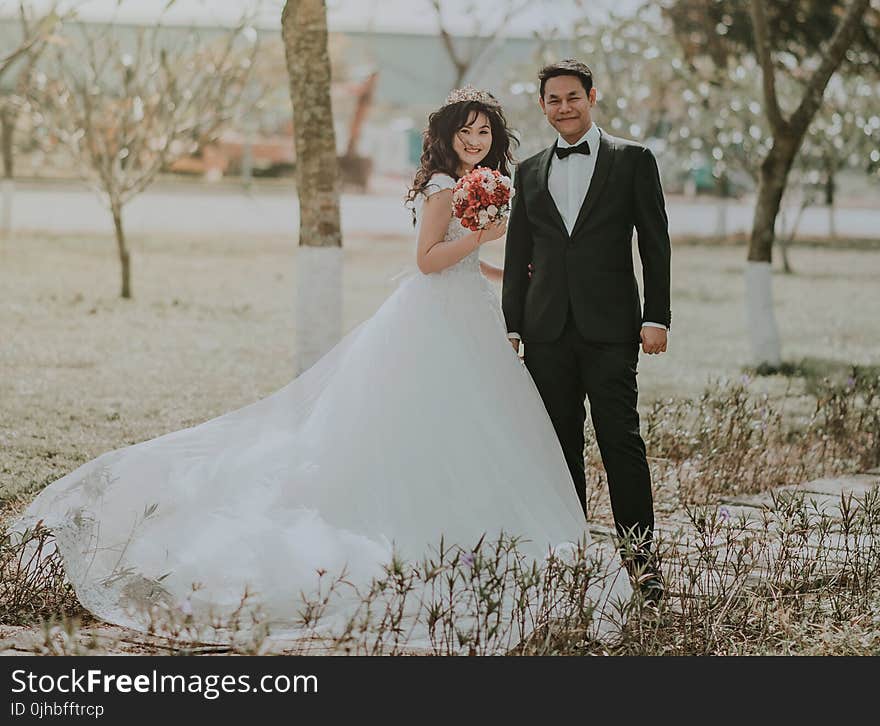 Woman Wearing White Wedding Ball Beside Man Wearing Black Notch-lapel Suit on Pathway Near the Green Grass Field