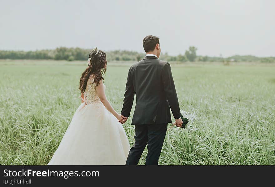 Woman in White Wedding Dress Holding Hand to Man in Black Suit