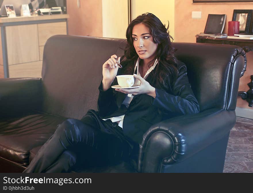 Woman in Black Blazer Holding Teacup While Sits on Black Sofa