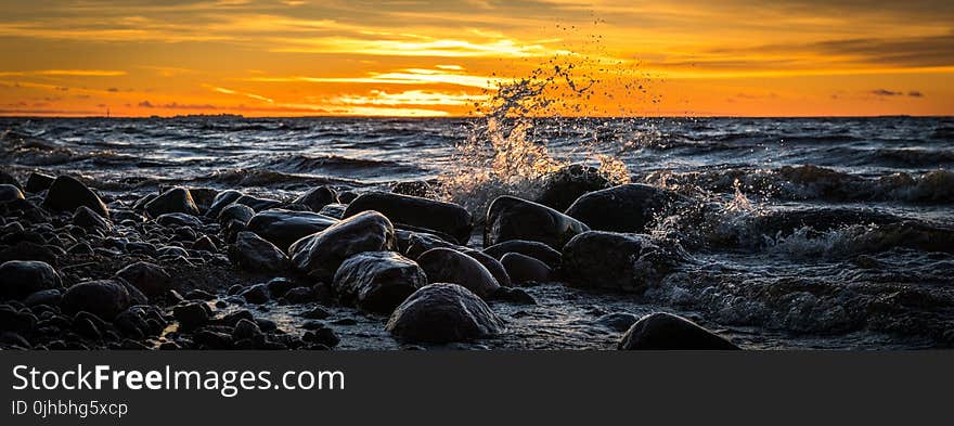 Waves Splashing at Stones on Beach during Sunset