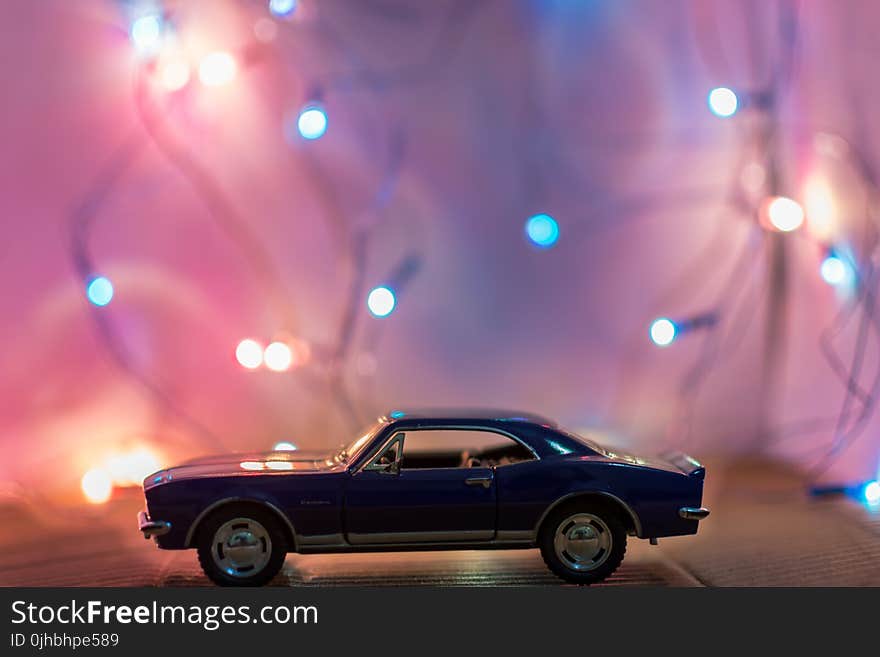 Selective Focus Photography of Classic Blue Coupe Die-cast Model in Front of String Lights on Table