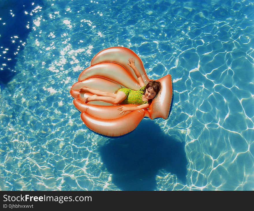 Girl Wearing Green Wet Suit Riding Inflatable Orange Life Buoy on Top of Body of Water