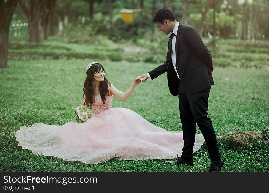 Man in 2-piece Suit Holding Woman in Peach-colored Wedding Gown White Holding Her Flower Bouquet