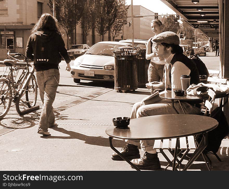 Man in Black and White Long-sleeved Shirt Sits on Brown Wooden Chair Facing Road