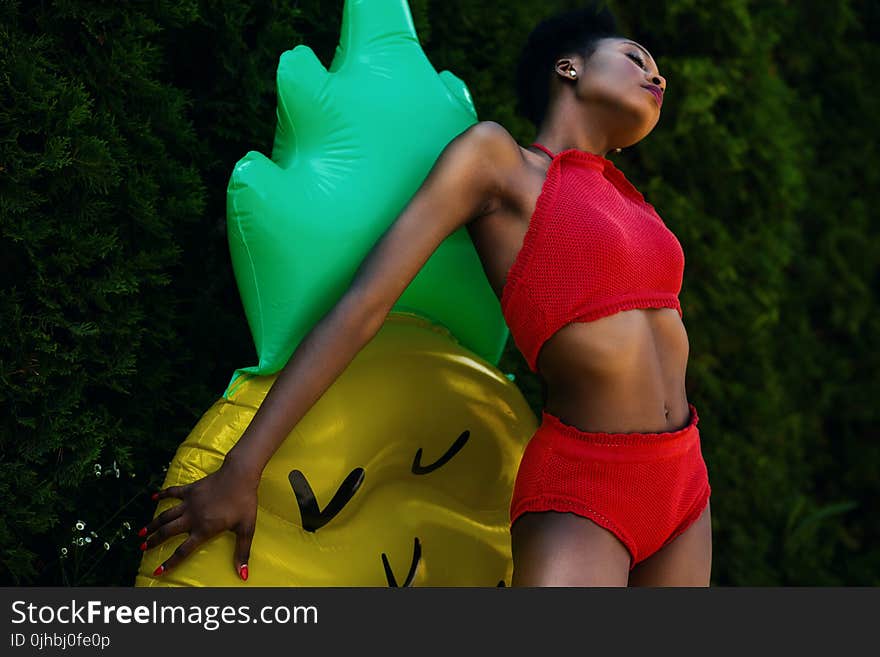 Woman Wearing Red Top and Bottoms Leaning on Yellow and Green Inflatable Standee