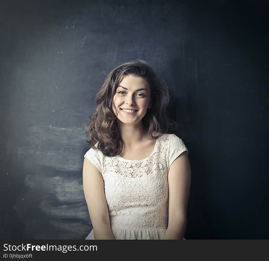 Brown Haired Girl in White Sleeveless Dress Standing Beside Black Painted Wall