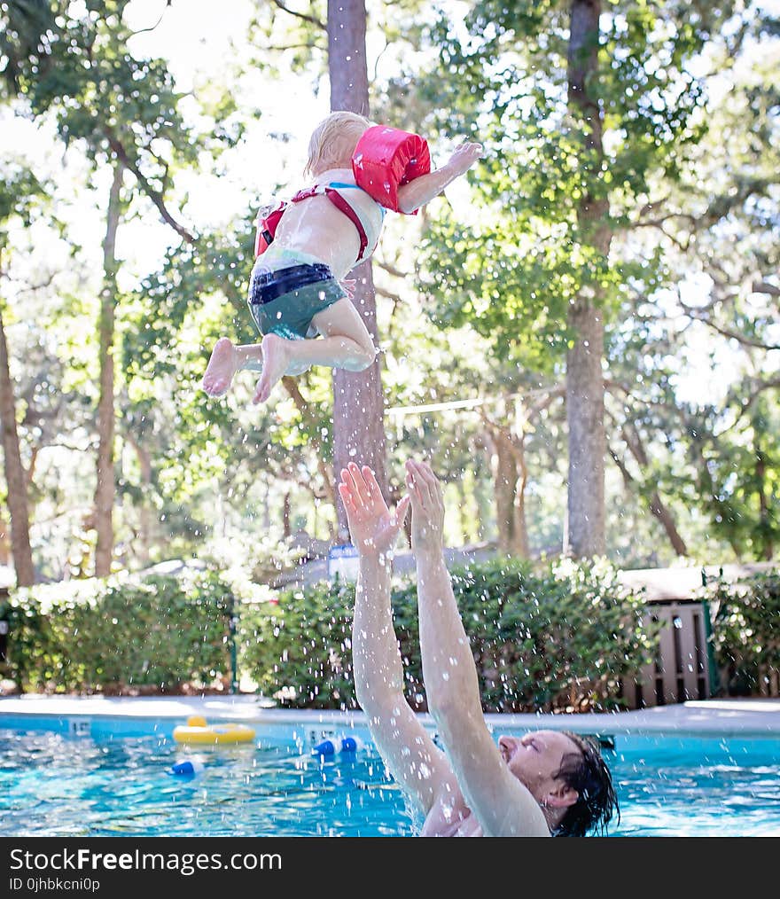 Photography of Man on Swimming Pool Tossing Toddler Above Pool