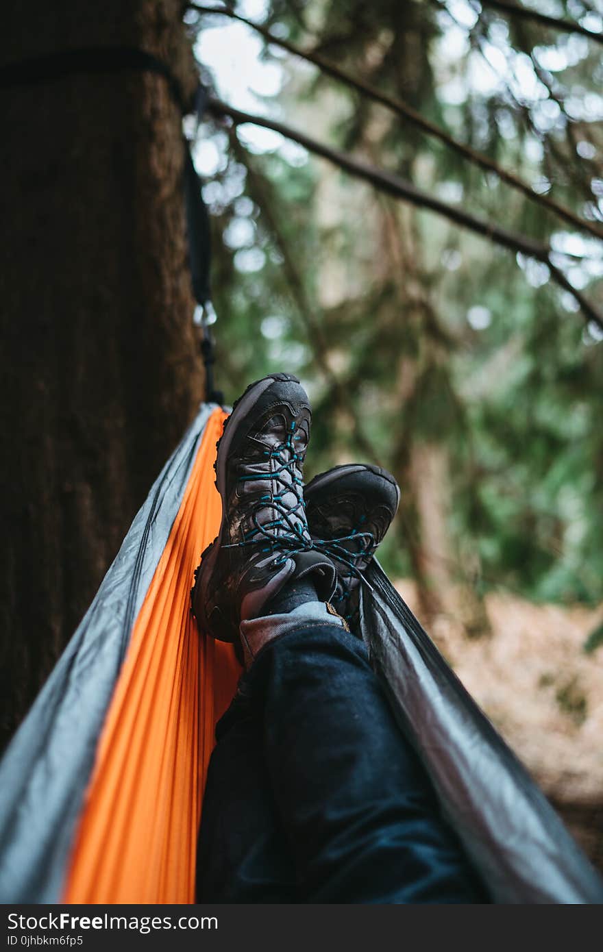 Person Wearing Pair of Black Hiking Shoes Lying on Orange and Gray Hammock