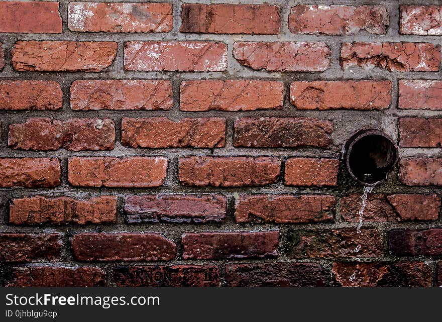 Round Brown Pipe Drainage With Liquid in Brown Bricked Concrete Wall