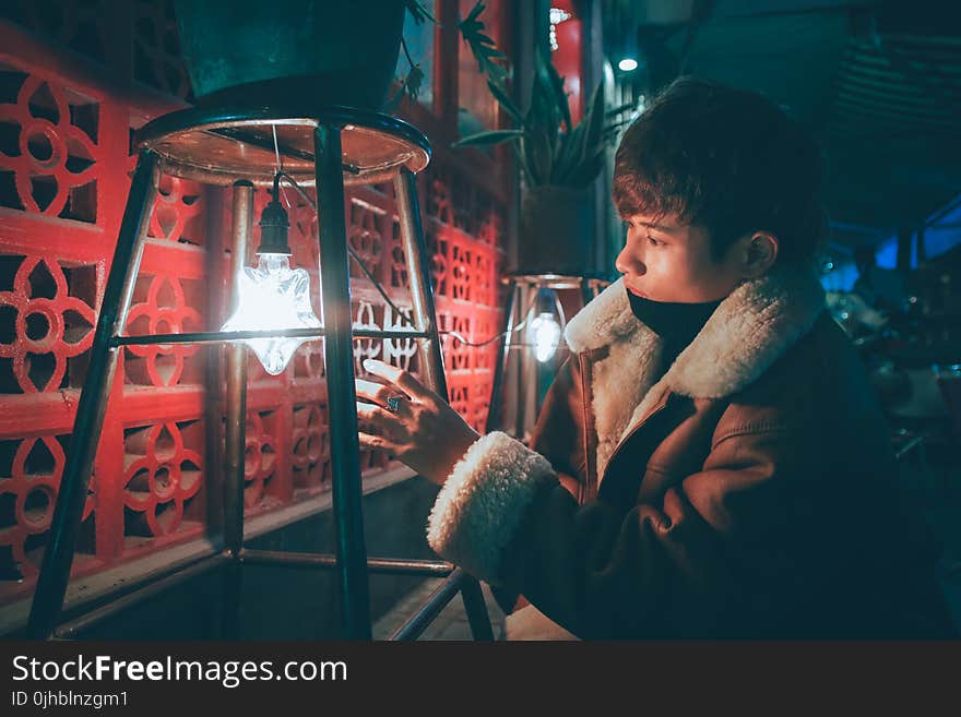 Man Wearing Brown and Gray Coat Reaching White and Black Light Bulb