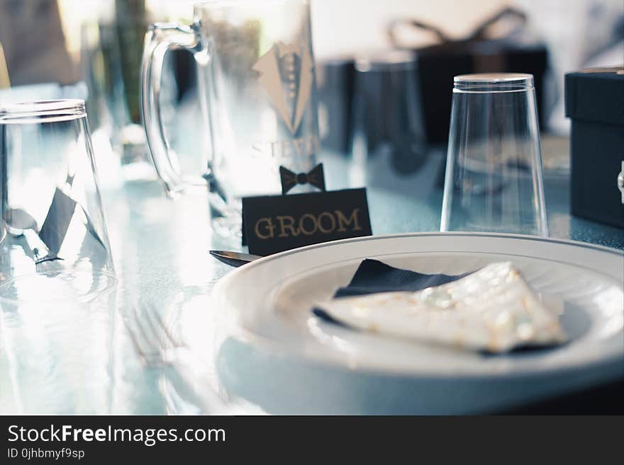 Round White Ceramic Plate Near Glass Cups and Groom Sign