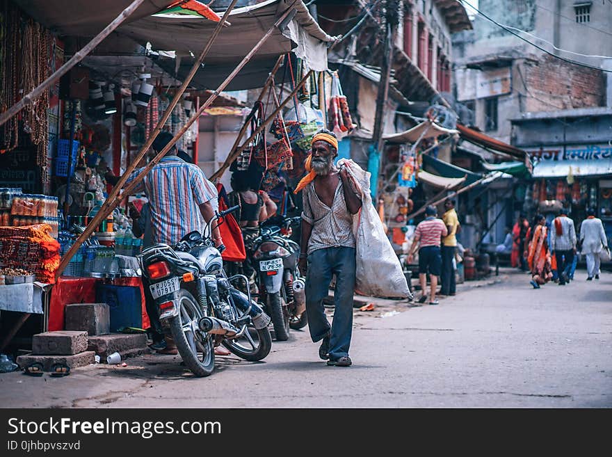 Man Holding White Sack Walking Beside Street Stores