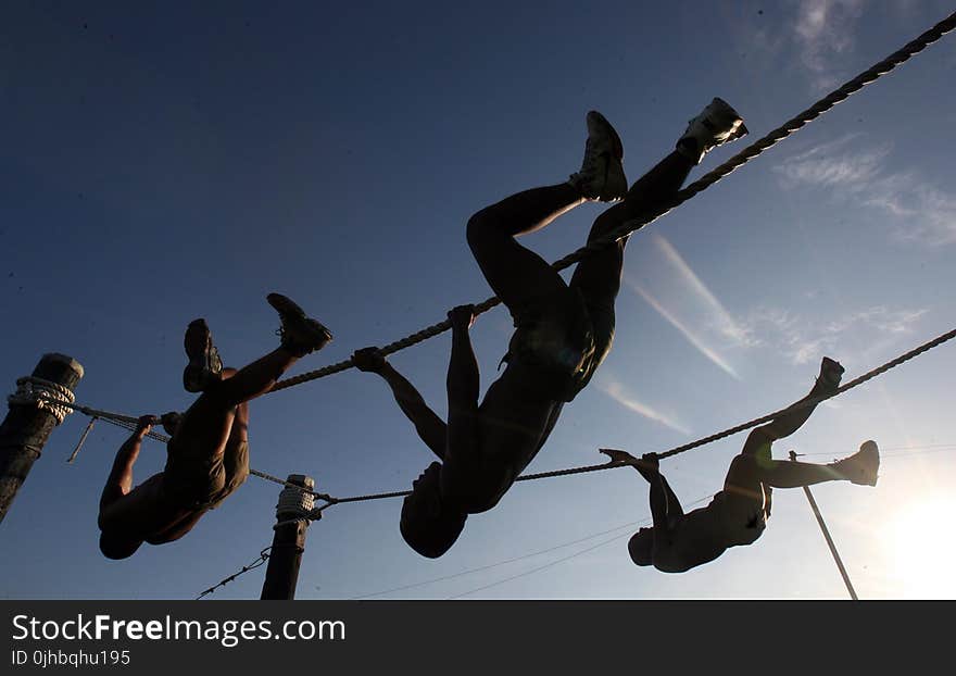 Three Man Climbing on Rope Under the Sunset