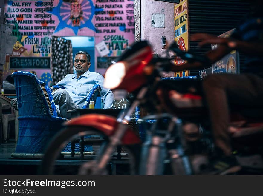 Man in Blue Dress Shirt Sitting on Blue Chair Beside Pink Painted Wall