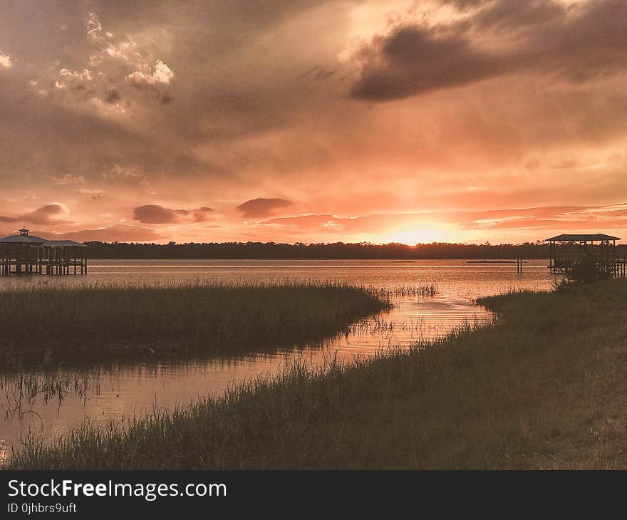 Grass Field Beside Body of Water during Sunset