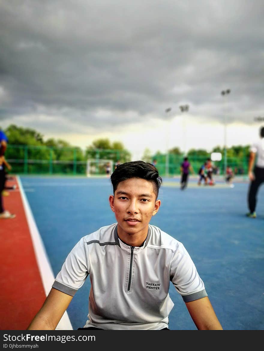 Tilt Lens Photography of Man Sitting Near Soccer Field during Cloudy Day