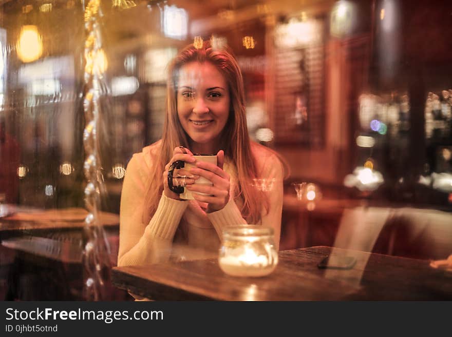 Woman Holding White Ceramic Cup Sitting Near Brown Wooden Table