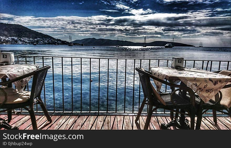 White Table With Two Armchair Set Near Body of Water and Mountain