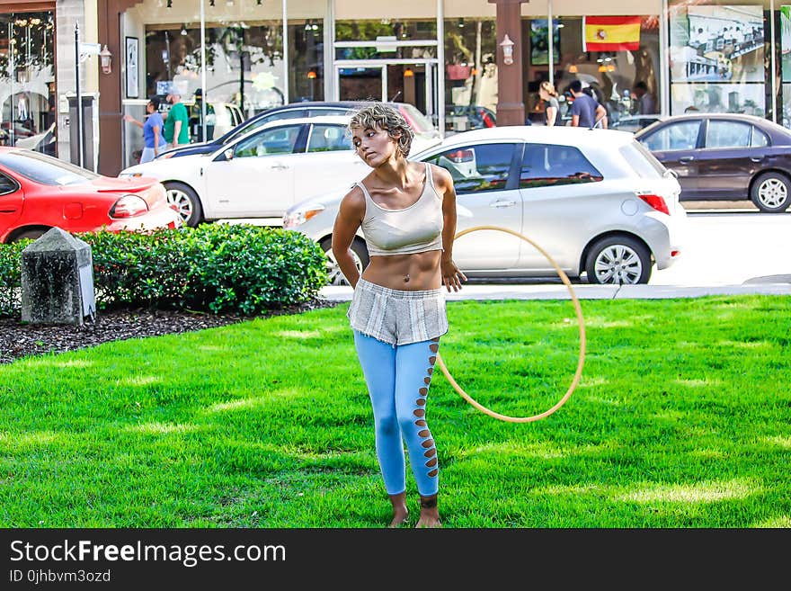 Woman in White Sleeveless Shirt and Blue Pants Holds Yellow Hula Hoop Stands on Green Grass