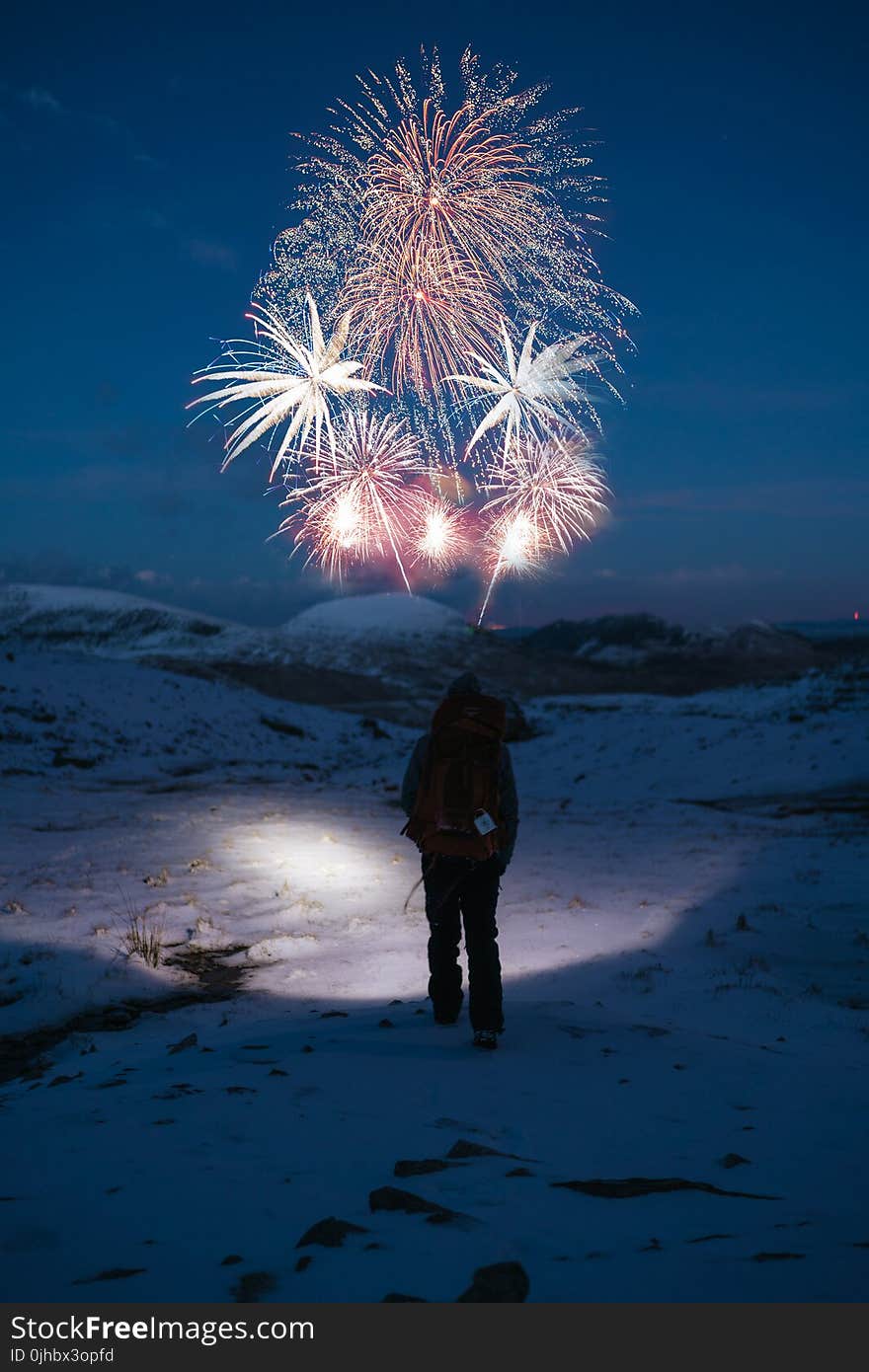 Person Stands on Snow Covered Mountain Looking at Fireworks