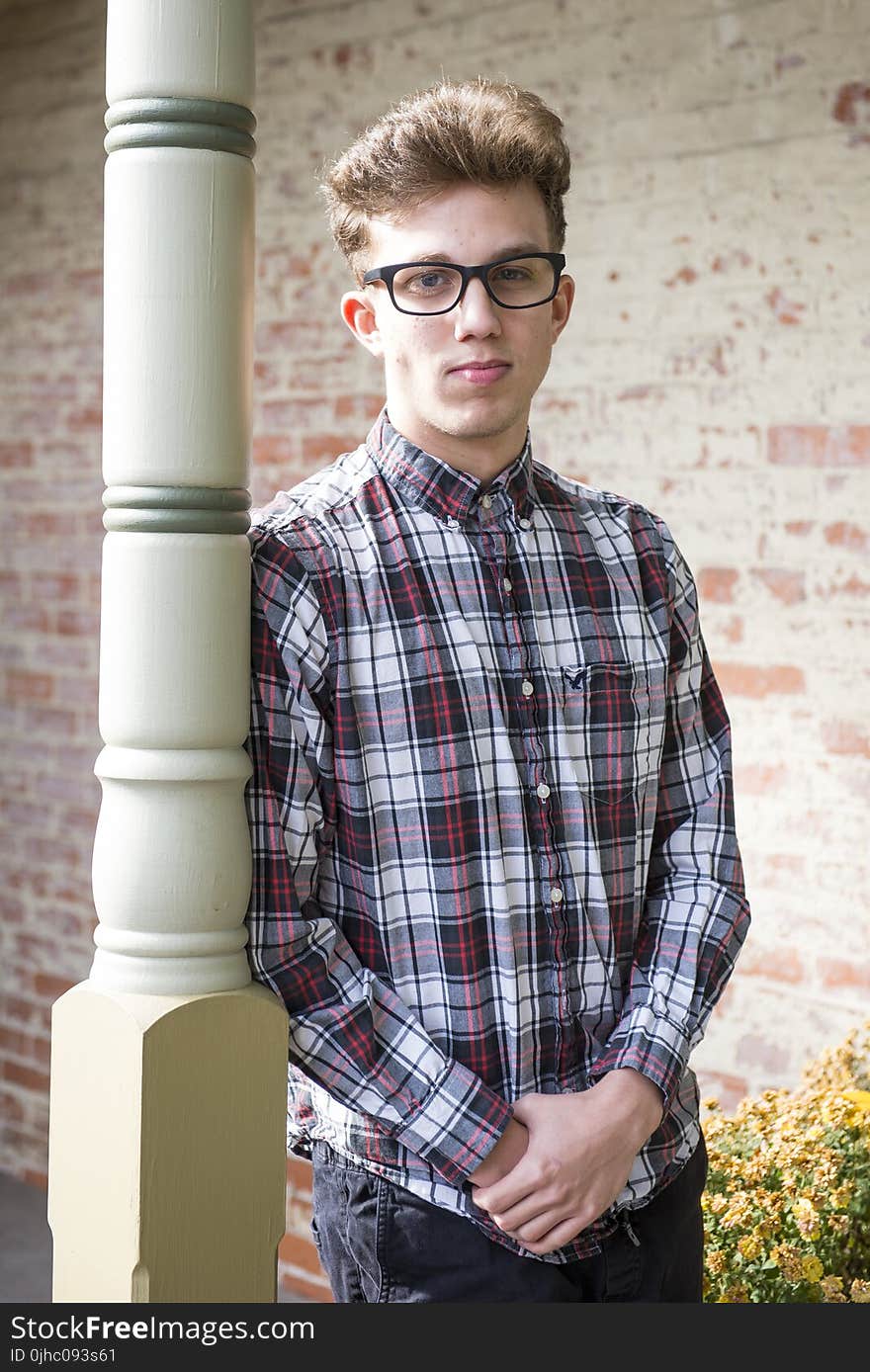 Man in Red Black and White Plaid-printed Dress Shirt Wearing Wayfarer Eyeglasses Leaning on White Wooden Post