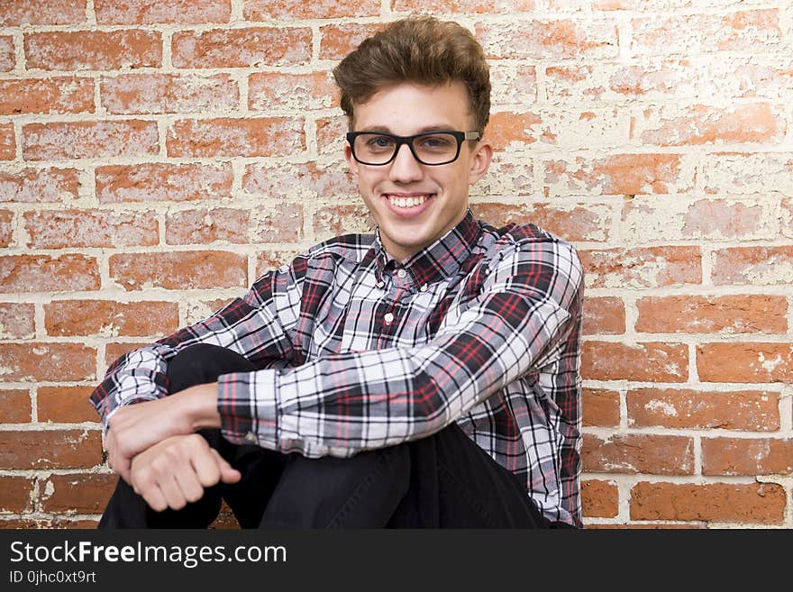 Man Wearing Plaid Dress Shirt And Black Pants Sitting Near Brown Brick Wall