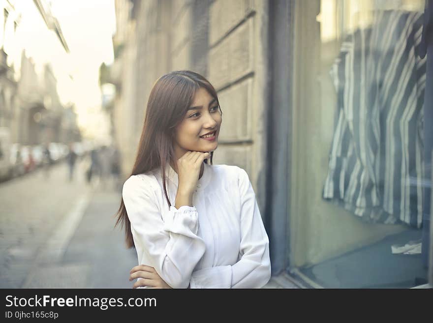 Focus Photo of Woman in White Long-sleeved Dress Standing at the Front of Gray Building