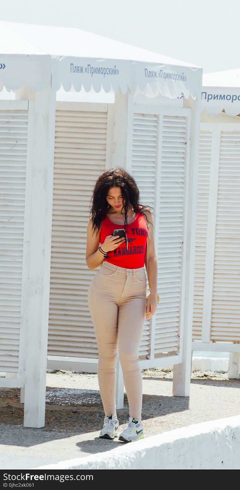 Woman in Red Tank Top and Gray High-waist Jeans Standing Near Wooden Cabinet