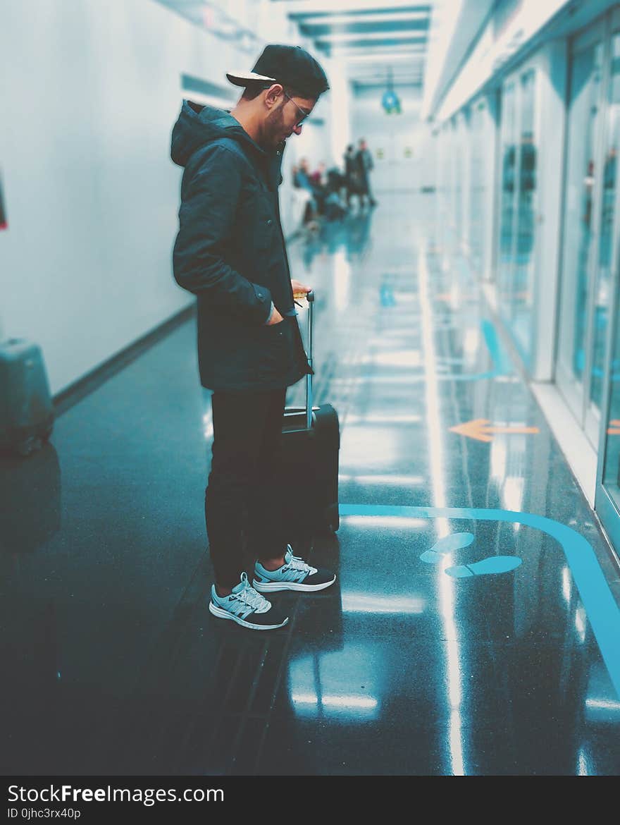 Man Stands Front of Glass Panel While Holding Luggage