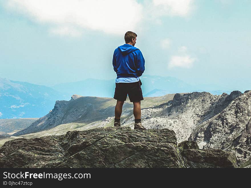 Man Wearing Blue Hoodie Standing on Top of Mountain