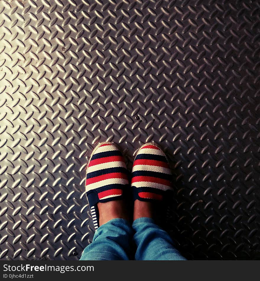 Person Wearing Red-and-multicolored Slip-on Shoes Standing on Gray Metallic Diamond Plate