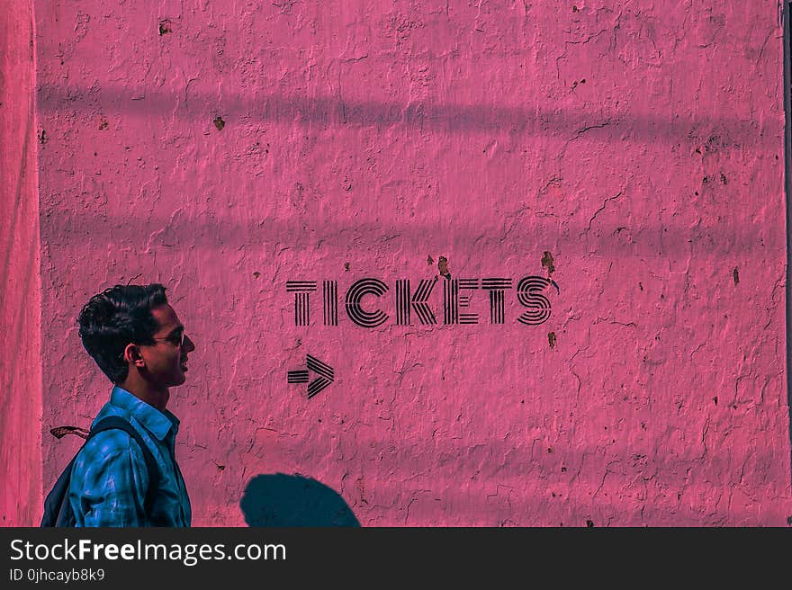 Man Wearing Blue Sports Shirt and Backpack Passing Through Pink Wall