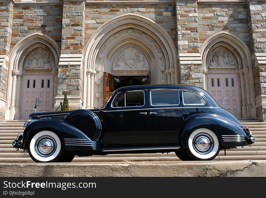 Classic Black Car Parked In Front Of Grey Concrete Building