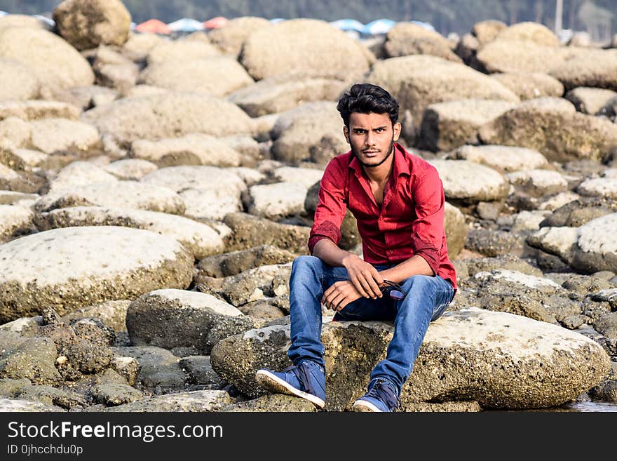 Man Wearing Red Dress Shirt and Blue Jeans White Sitting on Gray Stone Formation