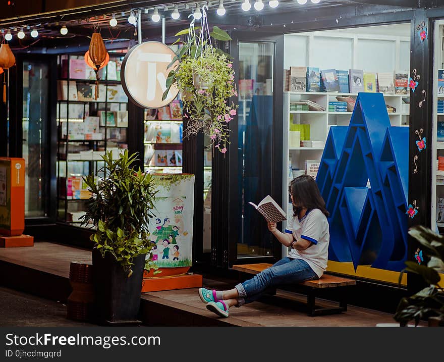 Woman Sitting Down On Bench And Reading Infront of Store