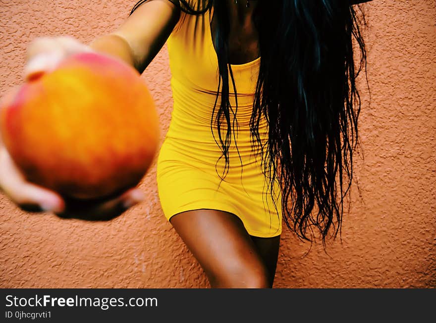 Woman Holding Round Fruit While Leaning on Orange Wall