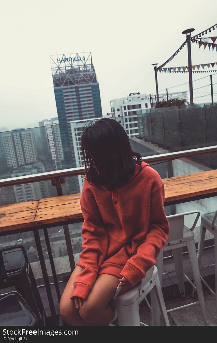 Photograph of Woman Wearing Red Pullover Hoodie Jacket Sitting on White Barstool