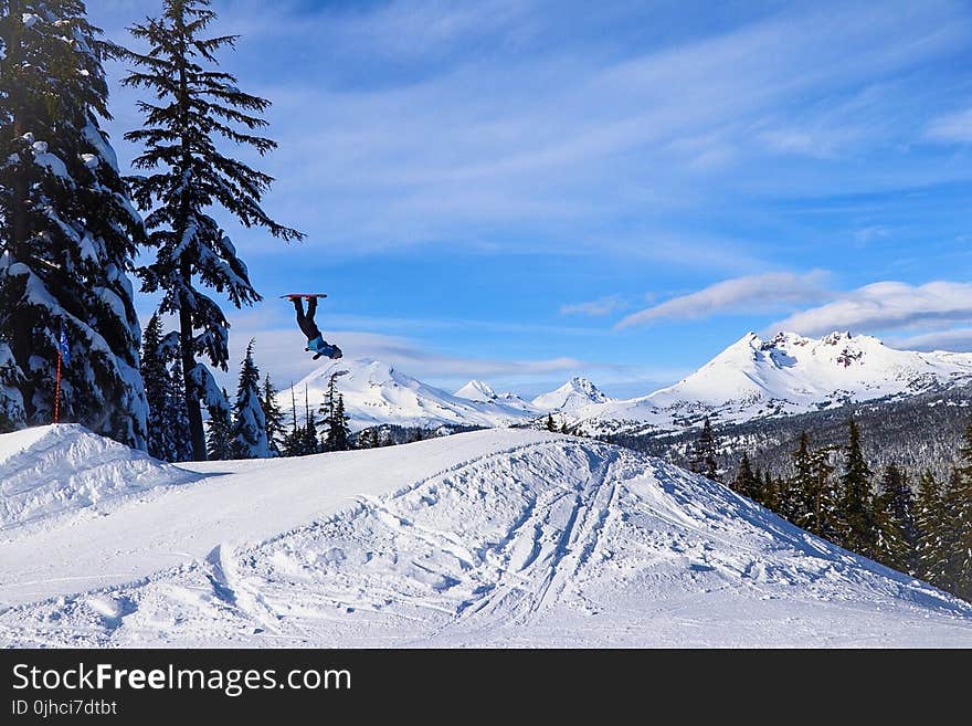 Person Doing Tricks In Mid Air Using Snowboard On Snowfield Mountain