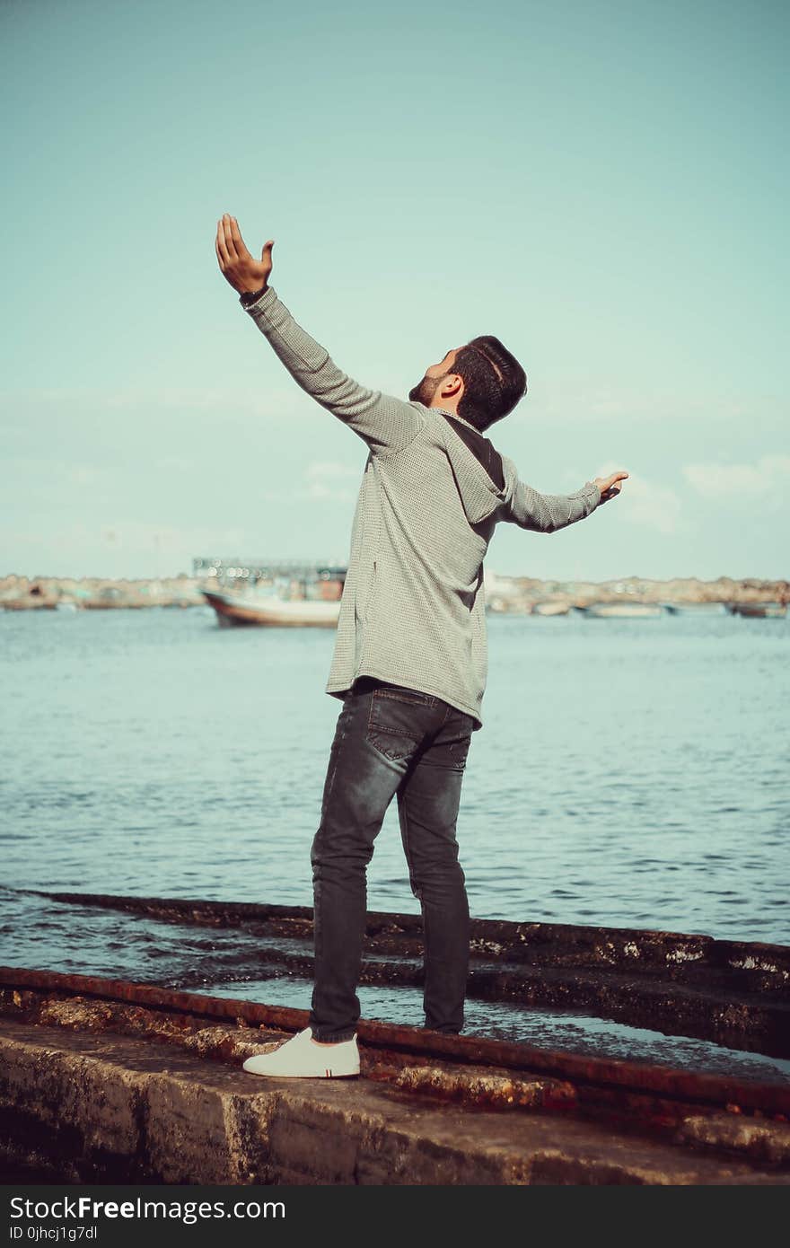 Man In GrEy Hoodie Standing on Grey Pavement Near Sea