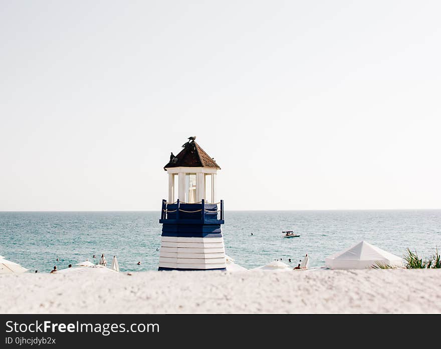 Photo of Blue and White Painted Lighthouse Near the Beach