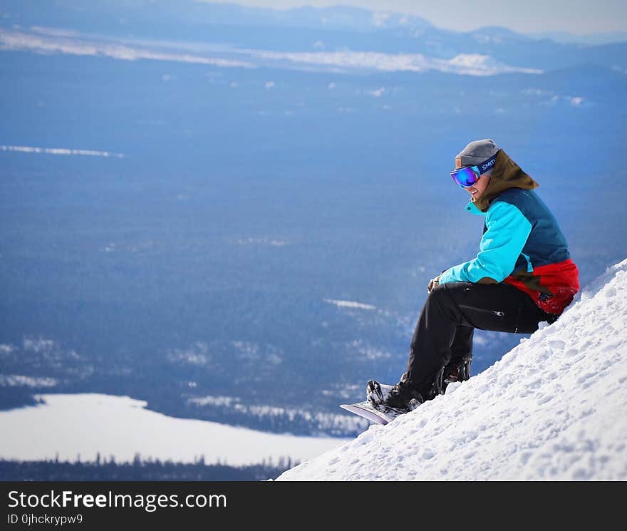 Person Wearing Blue and Red Winter Jacket Sitting on White Snow Mountain