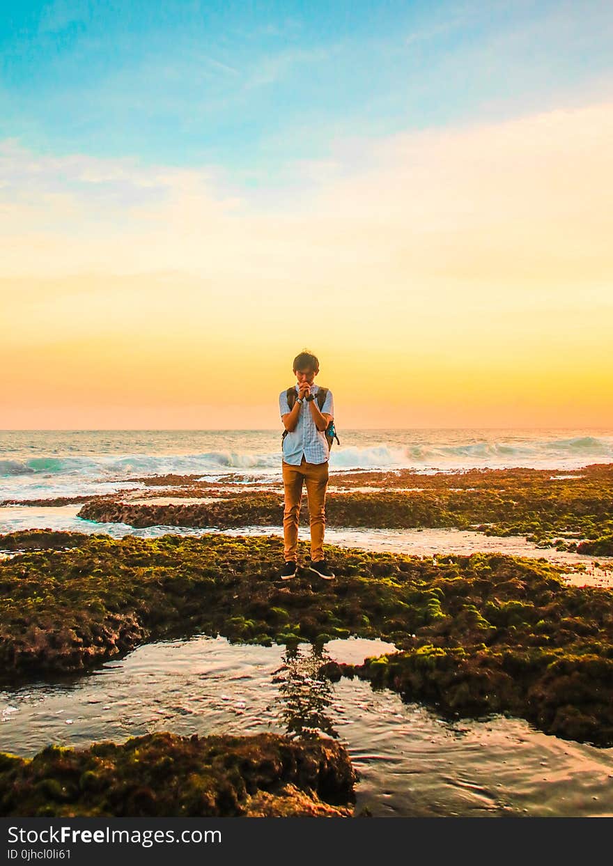 Man Standing on Rocks Near Beach during Golden Hour