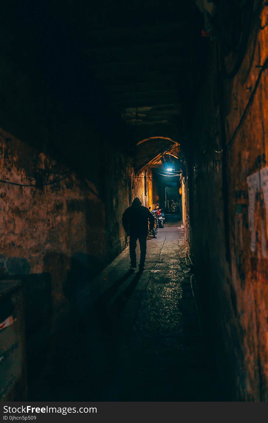 Photo of Person Walking Along Brown Wall Tunnel