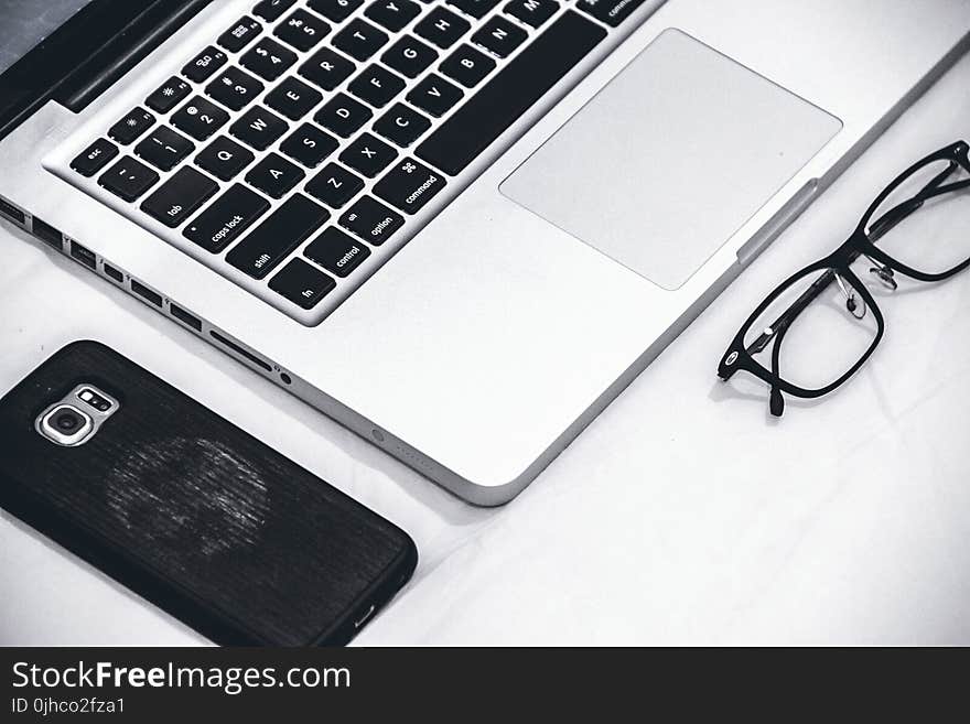 Macbook Beside Eyeglasses and Smartphone