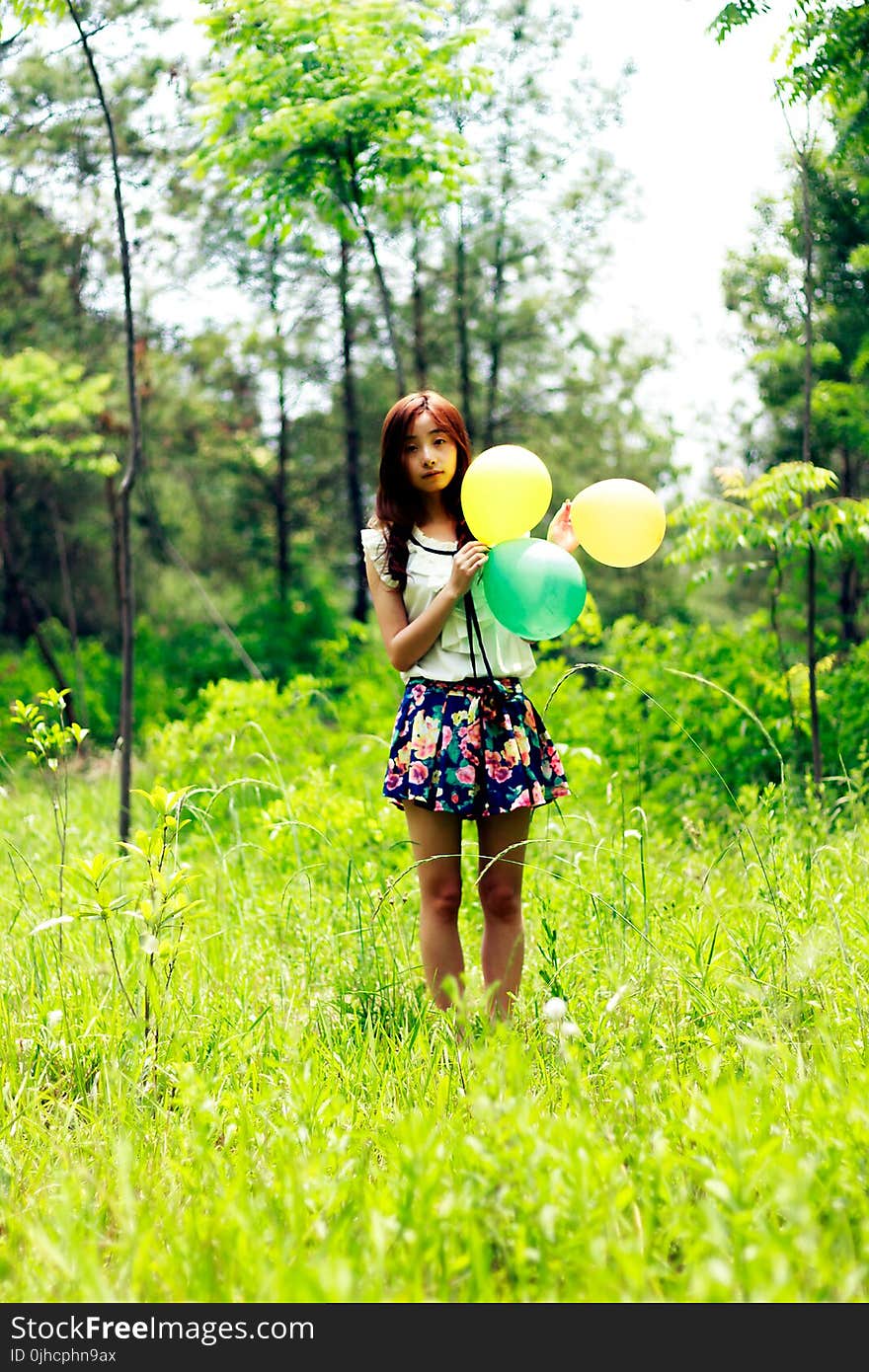 Woman Standing on Grass Field While Holding Three Balloons