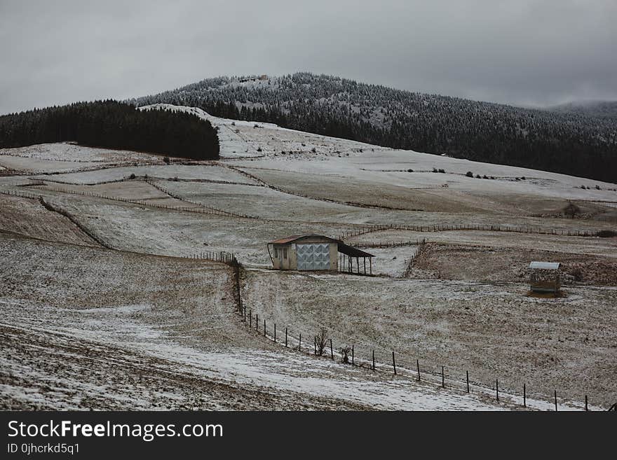 Brown Wooden House Surrounded With Brown Field Near Mountain Under Gray Sky at Daytime