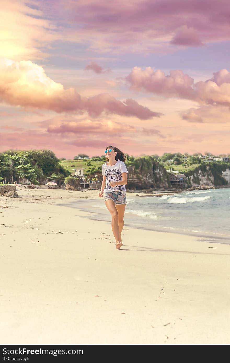 Smiling Woman Walking Barefood on Seashore Near Houses