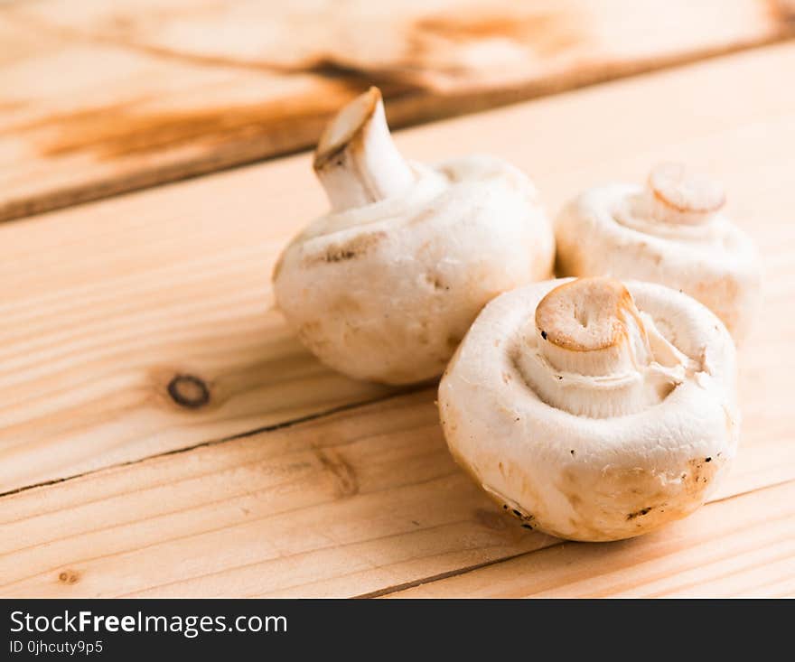 Three White Mushrooms on Beige Wooden Table