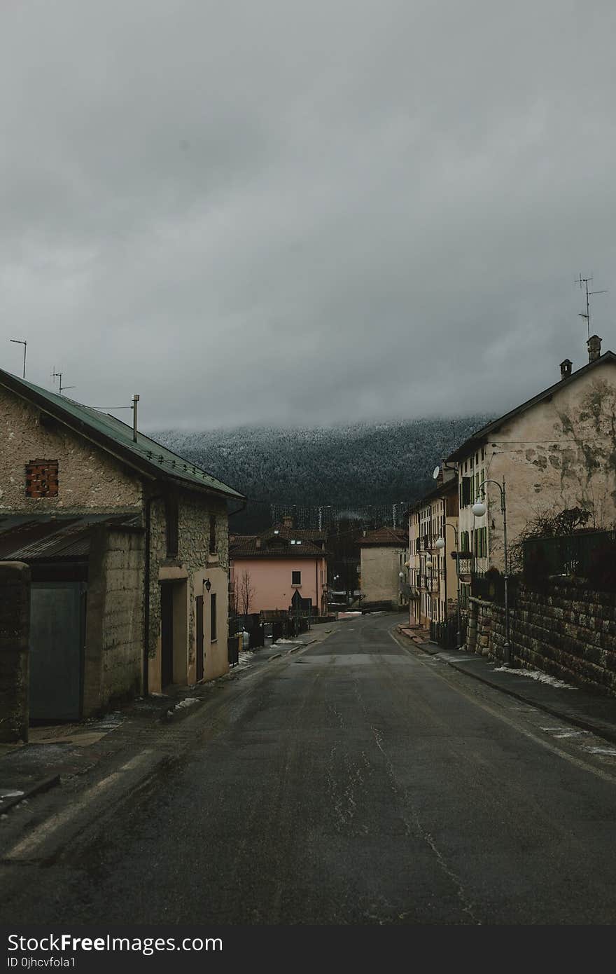 Gray Road Surrounded With Concrete Houses With Background of Dark Clouds