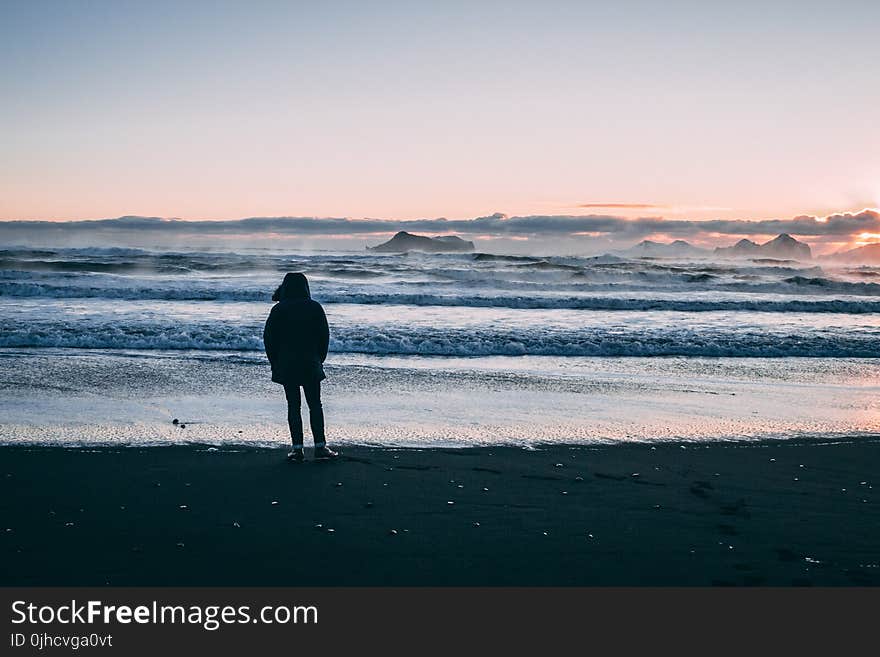 Person Standing on Beach Seashore during Sunset